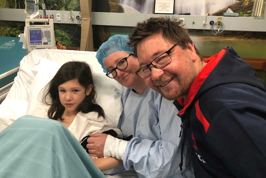 Lorelei in her hospital bed before transplant, with her mother Jenny and father Peter surrounding her.