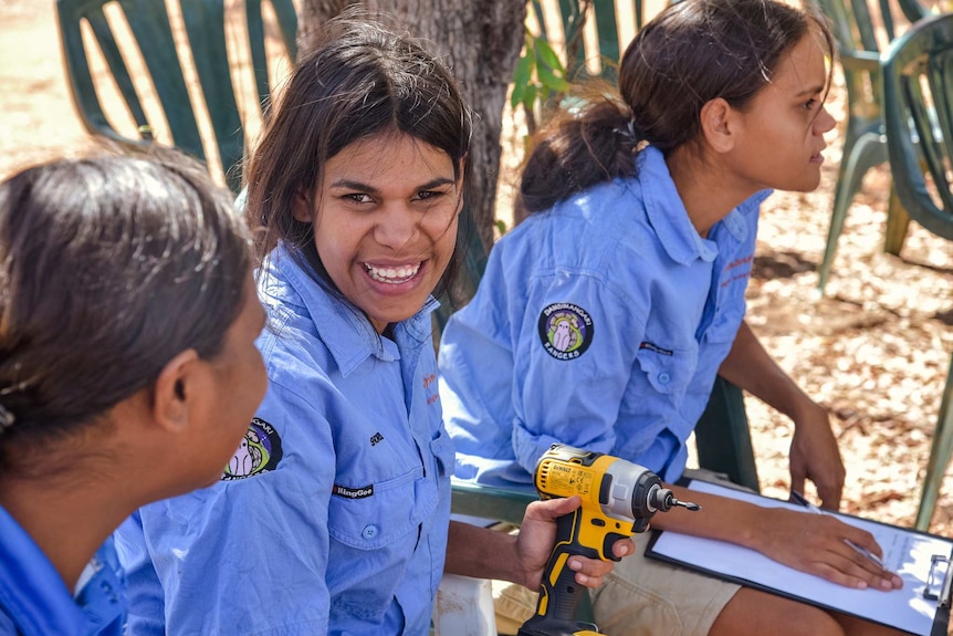 Three female rangers sitting in uniform listening to a presentation, one of them smiling at camera.