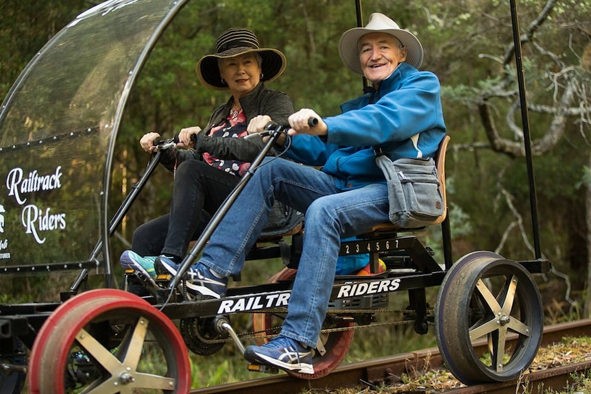 A man and a woman riding a rail buggy in a forested area.