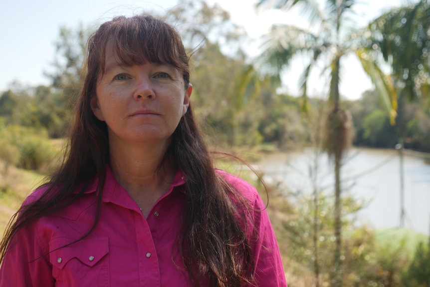 woman with long dark hair and wearing collared pink shirt, with creek in background