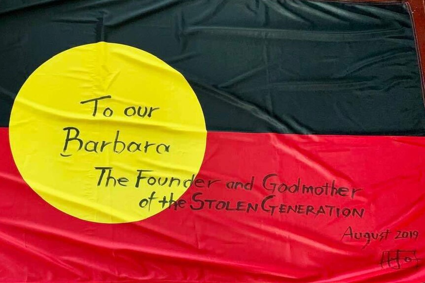 An Aboriginal flag with the words 'to our Barbara, the founder and Godmother of the stolen generation' written on it.