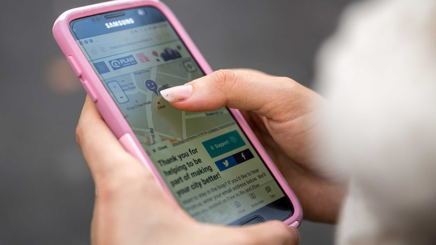 A young woman holds a phone showing Plan International's safety map