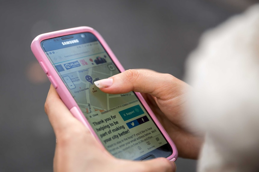 A young woman holds a phone showing Plan International's safety map