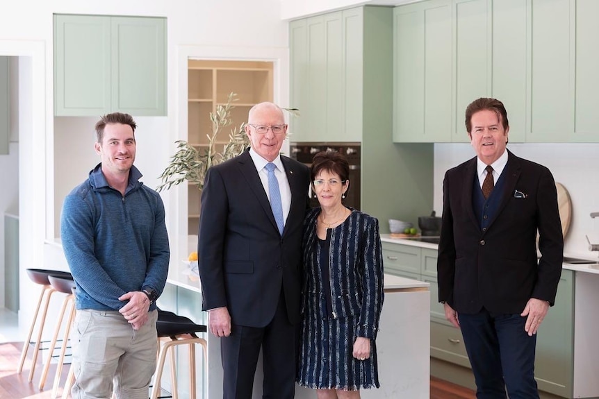 David and Linda Hurley smile in a kitchen standing alongsides a builder and a man in a suit