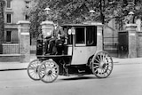 A 19th century man sits upon a carriage with a steering consul