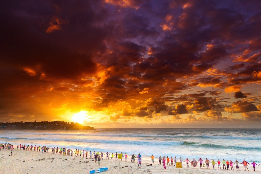 People wearing fluoro gathered at Bondi Beach at dawn for OneWave's fourth anniversary.