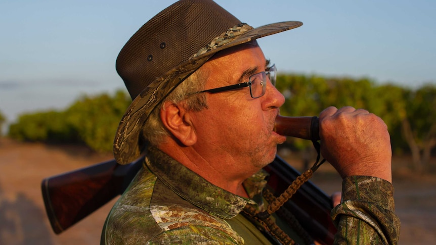 a man in a hat blows on a goose call.