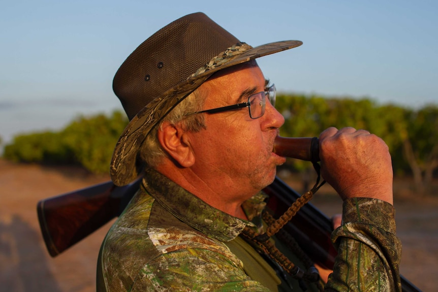 a man in a hat blows on a goose call