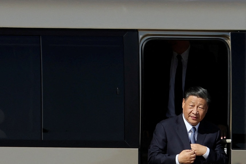 Xi Jinping dressed in a suit and tie steps out of a train.