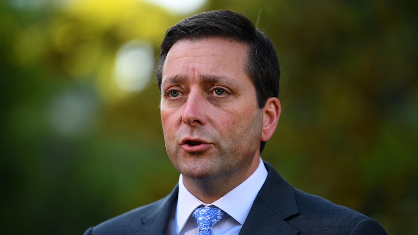 Victorian Opposition Leader Matthew Guy, who is wearing a suit. The background behind him is blurry and green.
