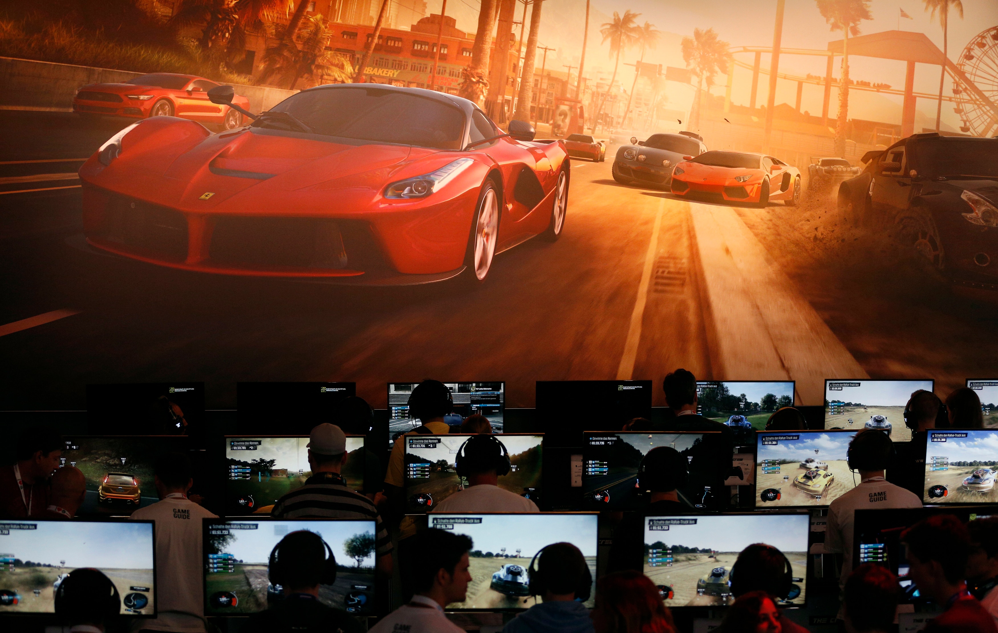 People wearing gaming headphones sit in front of monitors displaying race cars