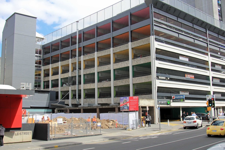 Piles of dirt with men in orange tops next to a mutli-level car park