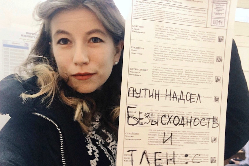 Close shot of a woman holding up a spoiled ballot paper to the camera.