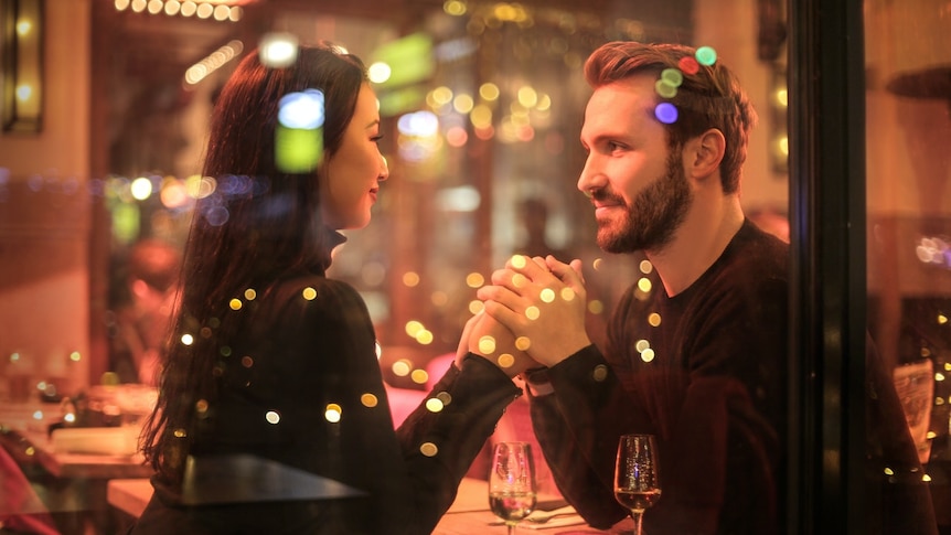 A couple holding hands across a table in a restaurant.