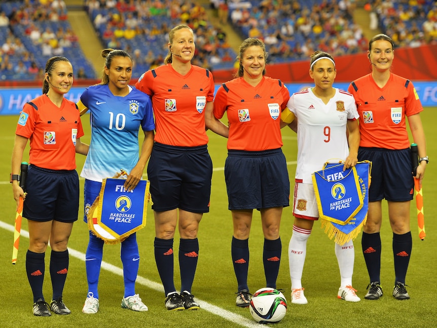 Two soccer players, one wearing blue and one wearing white, pose with referees before a big tournament match