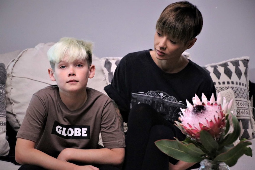 A mid shot of a woman with short hair and a black t-shirt sitting on a couch looking at a young boy with blonde hair.