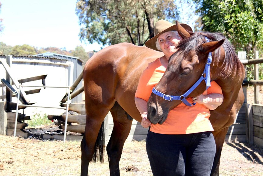 A woman stands with a horse in front of a burnt wooden fence.