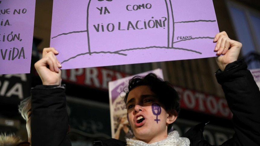 A woman holds a sign above her head and chants.