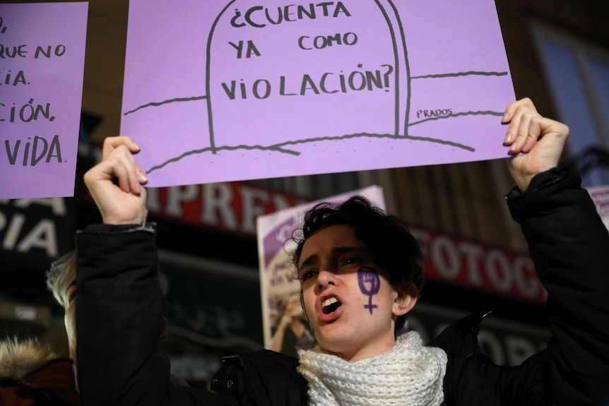 A woman holds a sign above her head and chants.