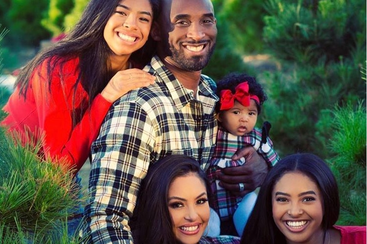 A smiling, happy family portrait taken with in front of a lush green background.