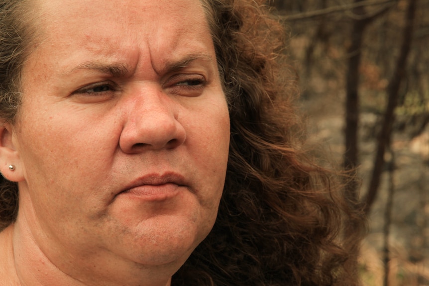 Close-up of woman looking out at burnt forest with a concerned look on her face.