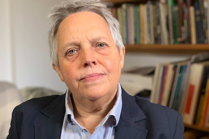 A woman in a navy blazer and blue shirt sitting in front of a bookcase