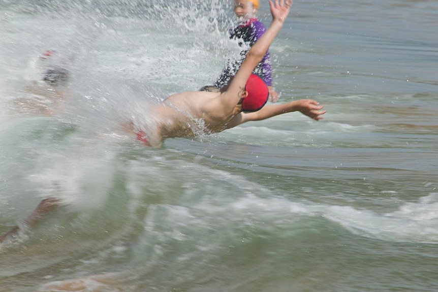 young surf lifesaver jumps sideways over a shorebreak wave