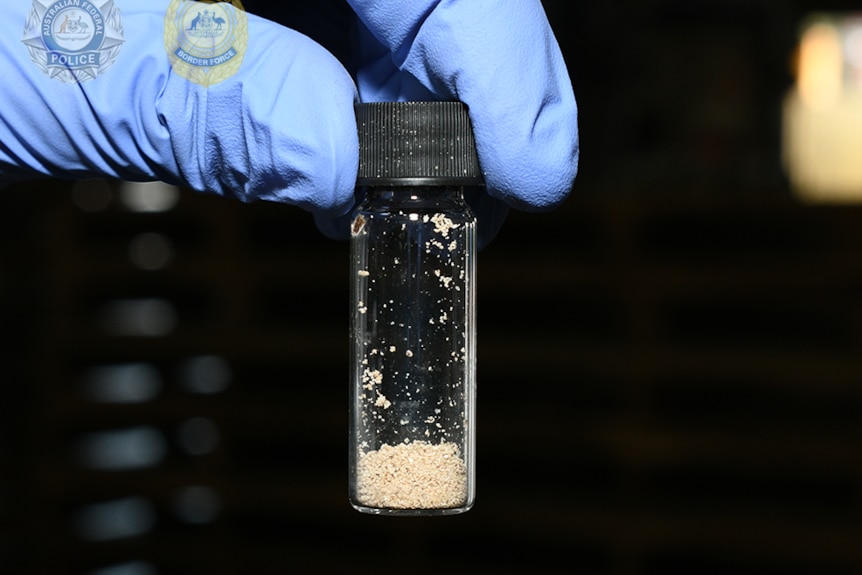 A gloved hand holds a tube filled with a grainy substance that is the drug fentanyl