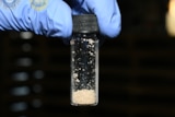 A gloved hand holds a tube filled with a grainy substance that is the drug fentanyl