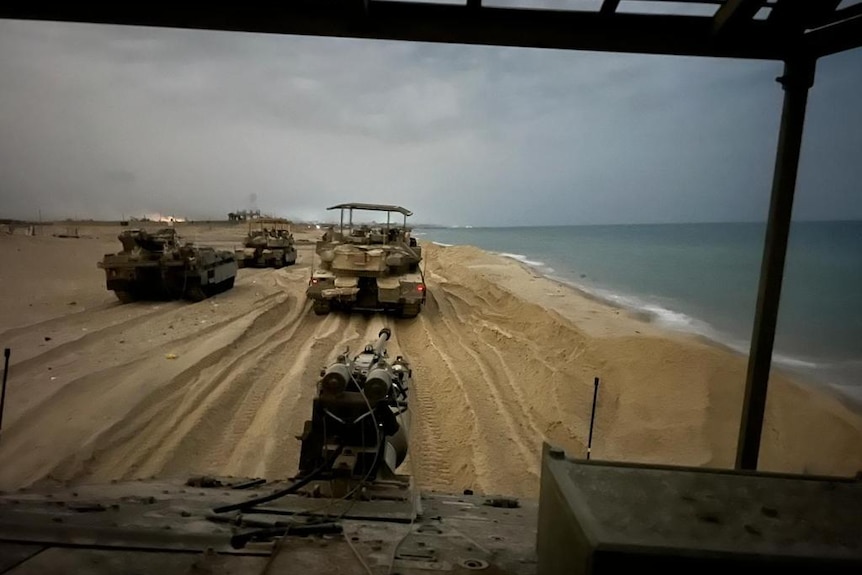 A photo shot from the perspective of an armoured vehicle showing tanks on a beach. 