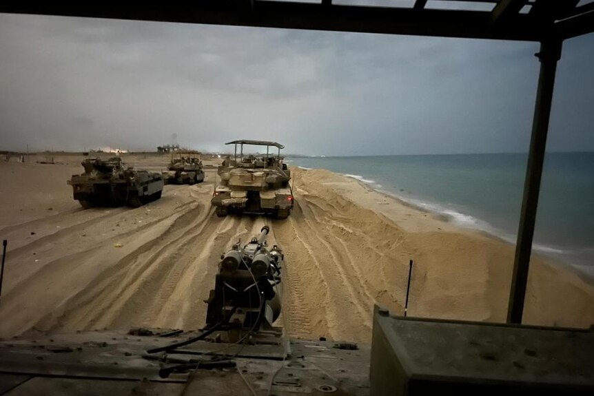 A photo shot from the perspective of an armoured vehicle showing tanks on a beach. 