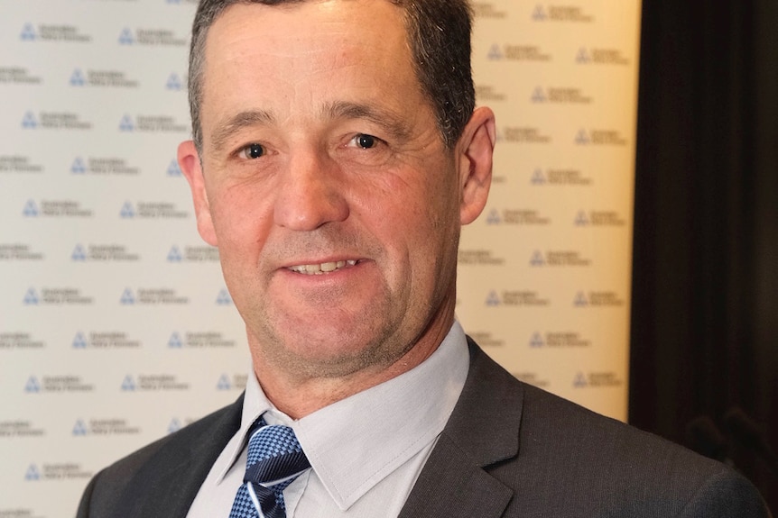 A portrait of a smiling man with dark hair and fair skin in a suit with a blue tie.