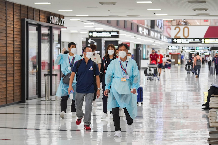 A group of Japanese officials in masks and blue gowns walk through Narita Airport 
