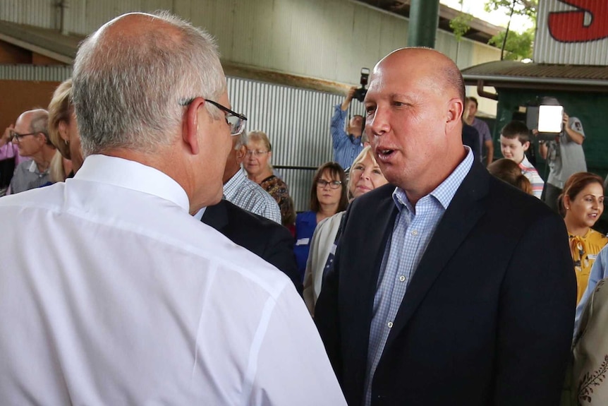 Peter Dutton shakes hands with Scott Morrison, seen from behind, at an election campaign event.