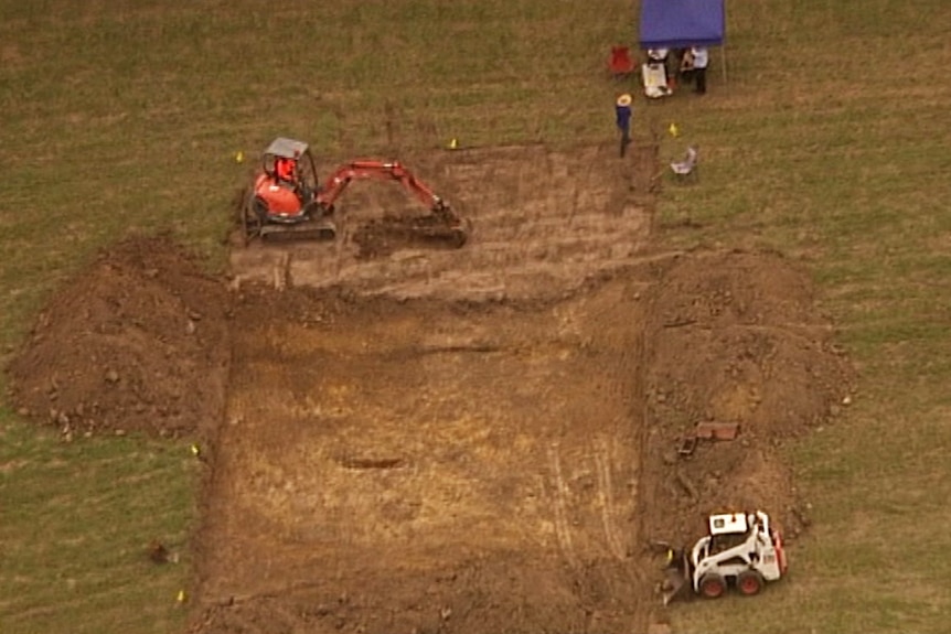 Aerial shot of digger excavating a field watched by police officers