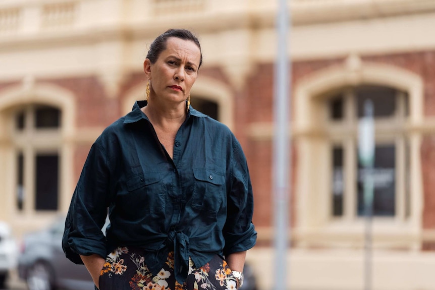 Woman stands with hands in pockets street in front of building