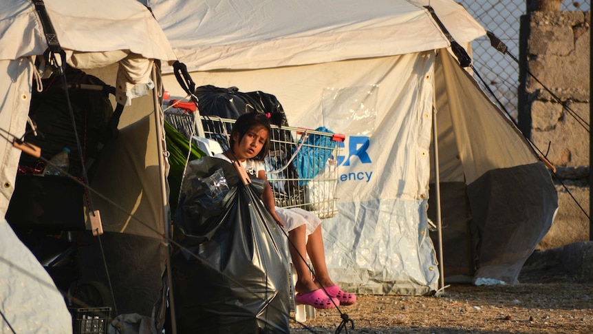 A child sits next to a shopping trolley stuffed with belongings at the new temporary refugee camp in Kara Tepe.