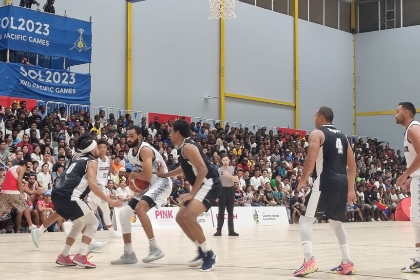 A guam basketballer is surrounded by three fijian basketballers, he craddles the ball in his arms