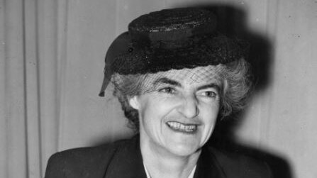 A black and white photograph of Dr Lucy Bryce wearing a suit and hat.