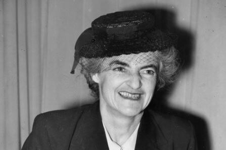 A black and white photograph of Dr Lucy Bryce wearing a suit and hat.