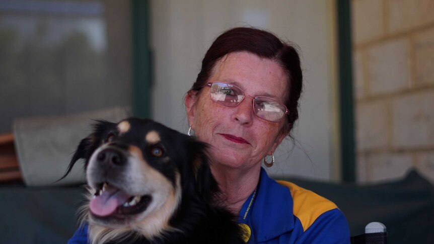 Rhonda Janetzki sits patting a dog. Her mouth forms a slight smile, while the dog has its tongue out.