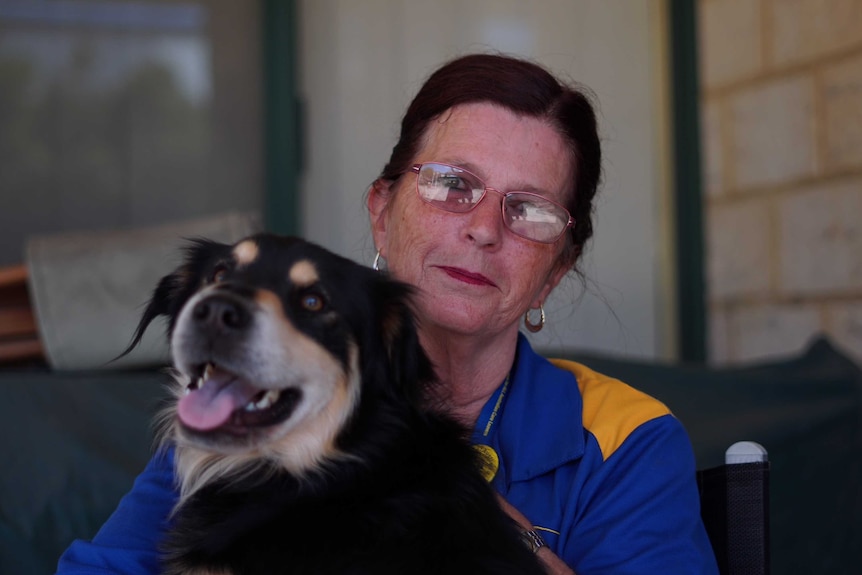 Rhonda Janetzki sits patting a dog. Her mouth forms a slight smile, while the dog has its tongue out.