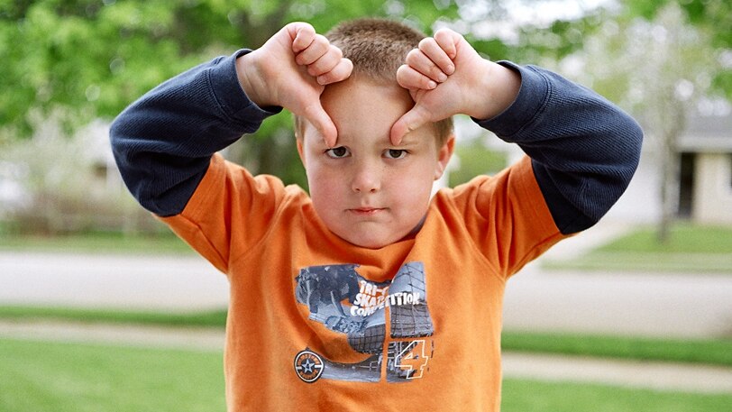 A young boy gives two thumbs down to the camera.