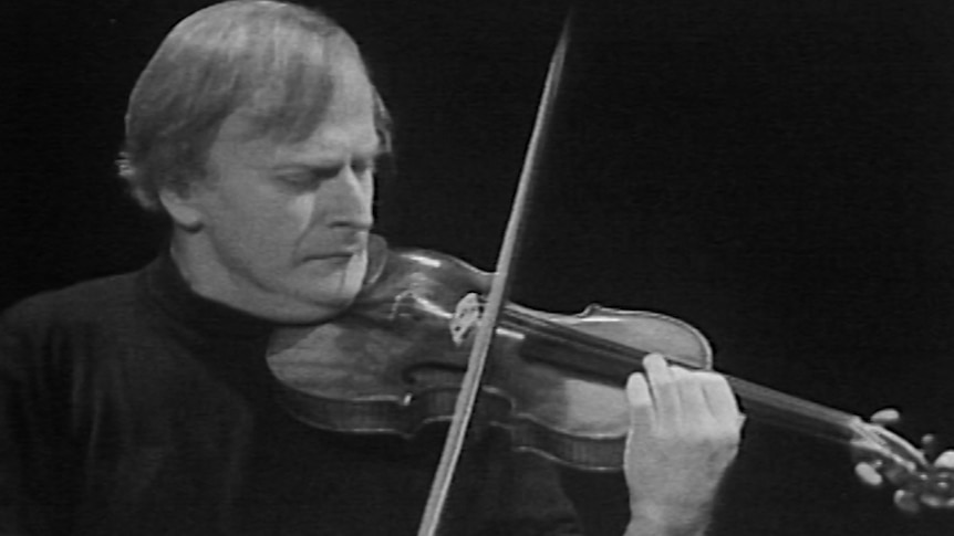 A black and white video still of a man playing a violin.