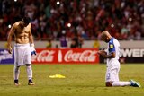 One Honduran player with his shirt of on the pitch and another on his knees praying.
