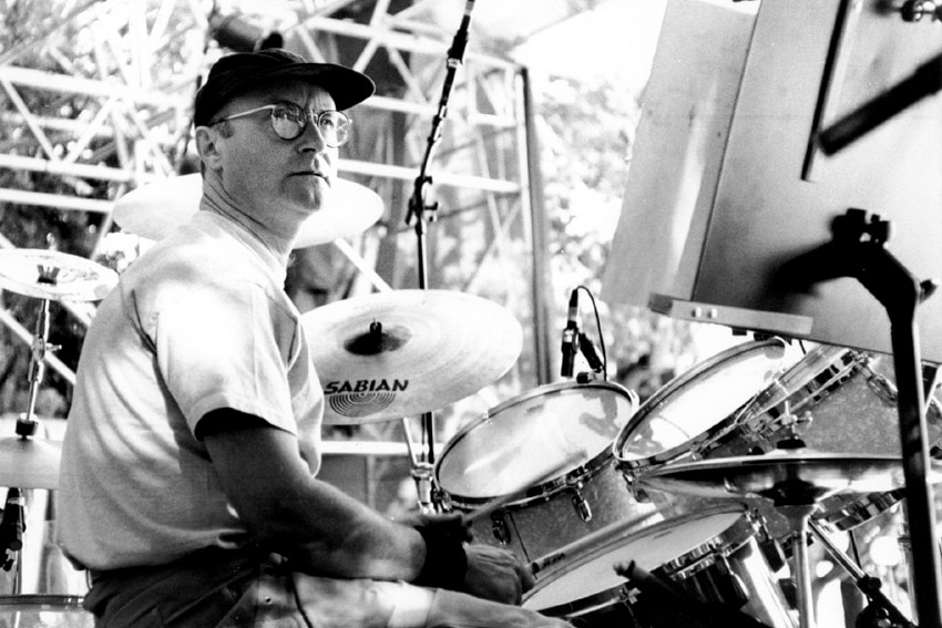 A man sits at a drum kit on stage.