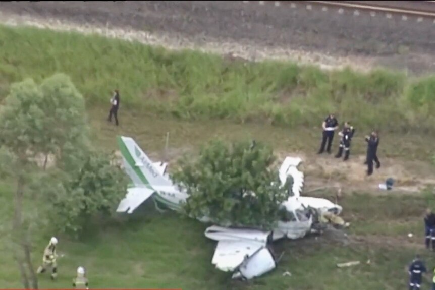 an aerial photo of a crashed plane covered in tree branches. police are standing around it