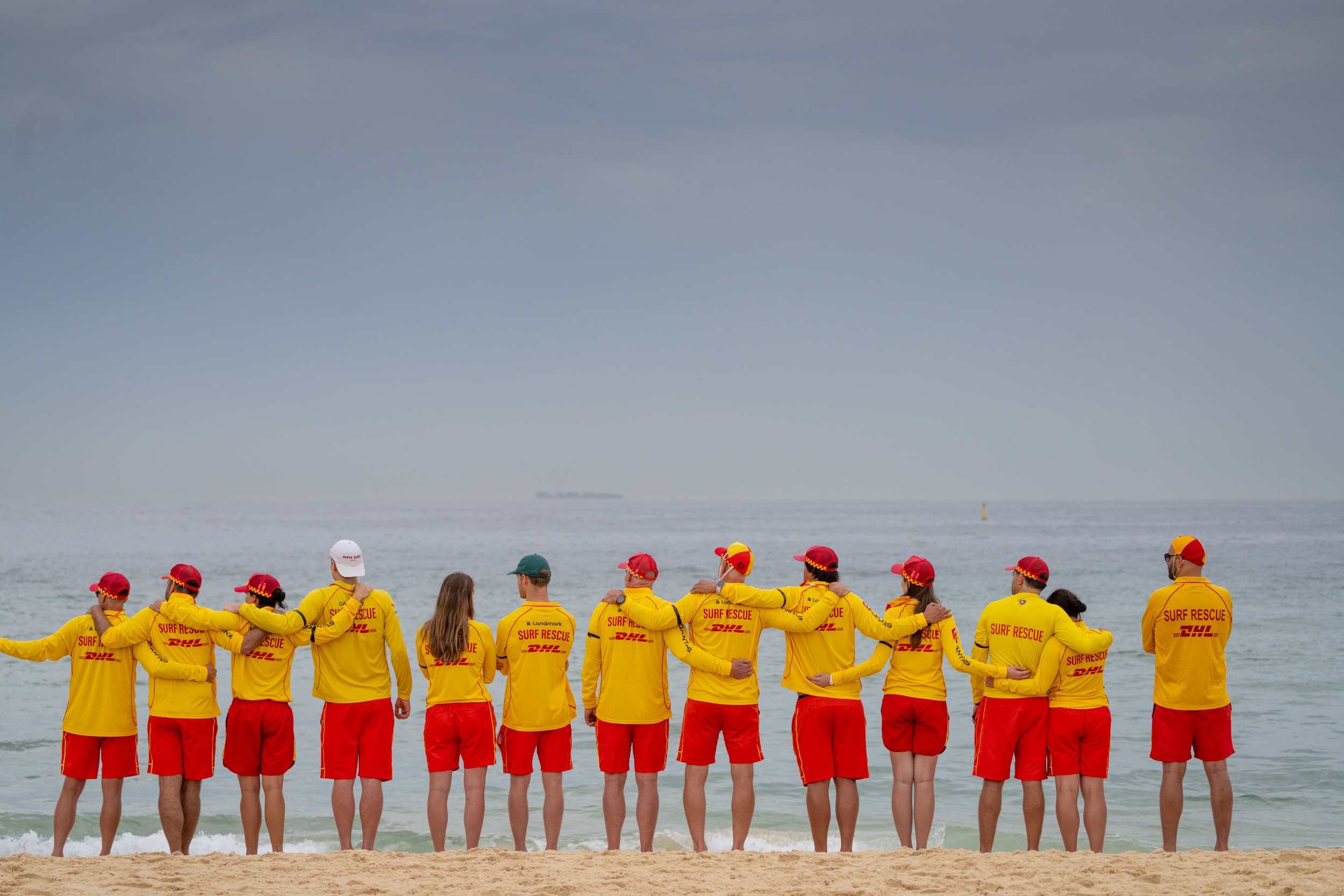 Uma fila de salva-vidas ao longo da praia, de frente para a água.