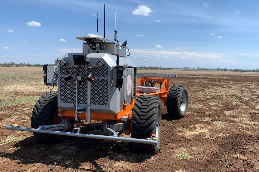 A grey and orange piece of machinery in a dry paddock.