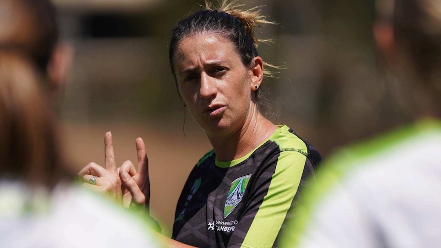 A female coach looks towards her players, while holding her fingers to demonstrate a move.